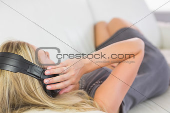 Casual attractive blonde lying on couch listening to music