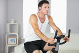 Attractive sporty man exercising on bike and listening to music