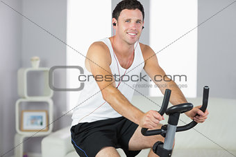 Smiling sporty man exercising on bike and listening to music