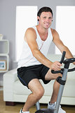 Cheerful sporty man exercising on bike and listening to music