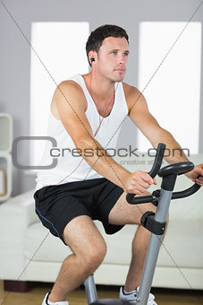 Handsome sporty man exercising on bike and listening to music