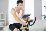 Smiling sporty man exercising on bike and using tablet