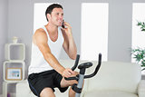 Smiling sporty man exercising on bike and phoning