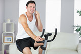 Cheerful sporty man exercising on bike and phoning
