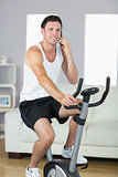 Content sporty man exercising on bike and phoning