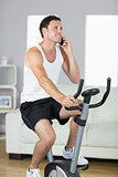Handsome sporty man exercising on bike and phoning