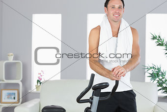 Smiling sporty man standing next to exercise bike