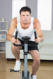 Handsome sporty man exercising on bike looking at camera