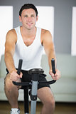 Handsome fit man exercising on bike smiling at camera