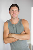 Sporty smiling man leaning against wall with arms crossed