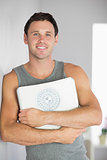 Sporty smiling man leaning against wall holding a scale