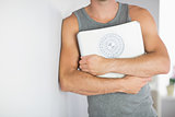 Sporty man leaning against wall holding a scale