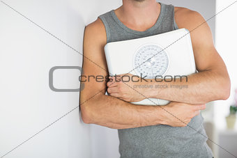 Sporty man leaning against wall holding a scale