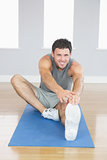 Smiling sporty man stretching his right leg
