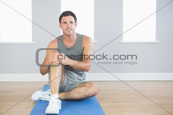 Smiling sporty man sitting on blue mat