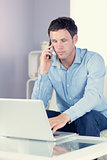 Attractive casual man using laptop and phoning