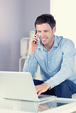 Smiling casual man using laptop and phoning