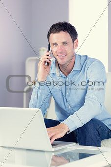 Cheerful casual man using laptop and phoning