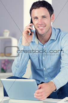 Smiling casual man holding tablet and phoning