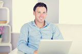 Smiling casual man sitting on couch using laptop