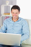 Cheerful casual man sitting on couch using laptop