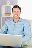 Happy casual man sitting on couch using laptop