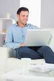 Laughing casual man sitting on couch using laptop