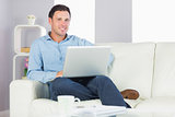 Content casual man sitting on couch using laptop looking at camera