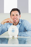 Smiling casual man putting coin in piggy bank