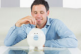 Content casual man putting coin in piggy bank