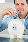 Attractive casual man putting coin in piggy bank