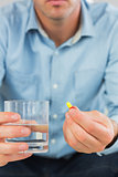 Close up of casual man holding a pill and glass of water