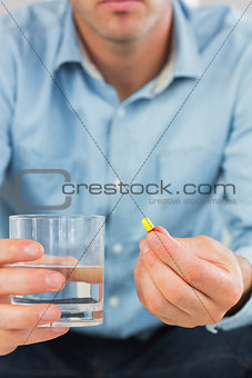 Close up of casual man holding a pill and glass of water