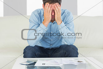 Troubled casual man sitting on couch covering his eyes paying bills