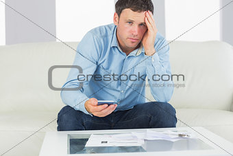 Upset casual man using calculator and looking at camera paying bills