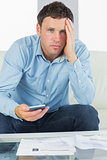 Worried casual man using calculator and looking at camera paying bills