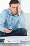 Worried casual man holding calculator paying bills
