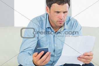 Serious casual man holding calculator paying bills looking at document