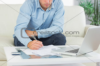 Close up of man writing on sheets paying bills