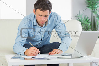 Serious casual man writing on sheets paying bills