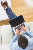 High angle view of casual man typing on laptop with feet on table