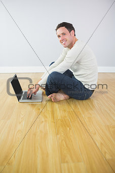 Casual smiling man sitting on floor using laptop