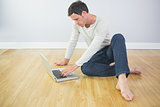 Casual calm man sitting on floor using laptop