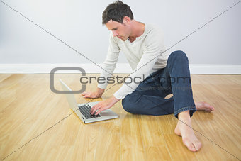 Casual calm man sitting on floor using laptop
