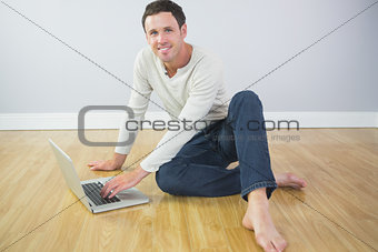 Casual cheerful man sitting on floor using laptop