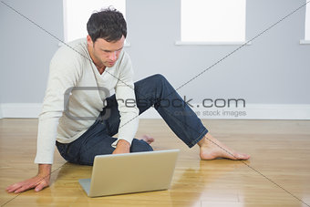 Casual good looking man sitting on floor using laptop