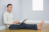 Casual smiling man leaning against wall using laptop