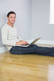 Casual cheerful man leaning against wall using laptop