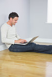 Casual laughing man leaning against wall using laptop