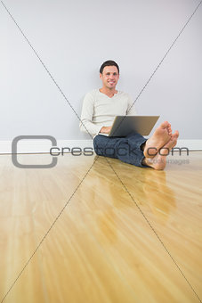 Casual content man leaning against wall using laptop
